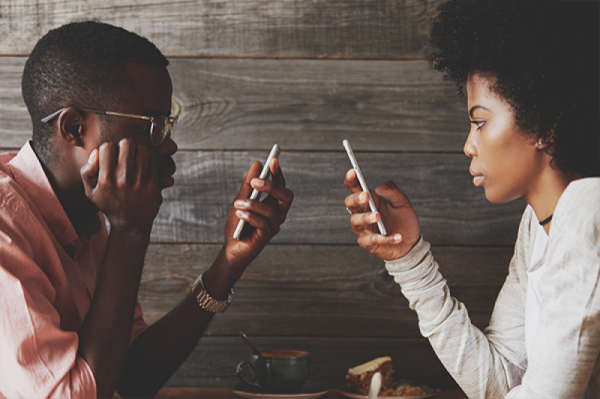 Two people, facing each other at table, holding up their smartphone in front of their face