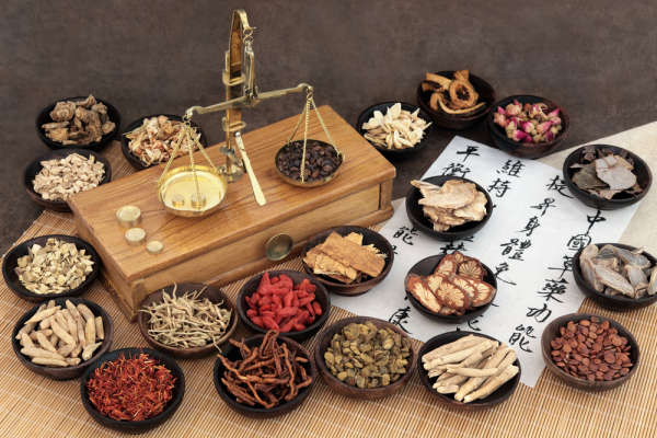 Chinese medicine ingredients with scales and calligraphy. Translation reads as Chinese herbal medicine as increasing the body's ability to maintain body and mind health and balance energy.