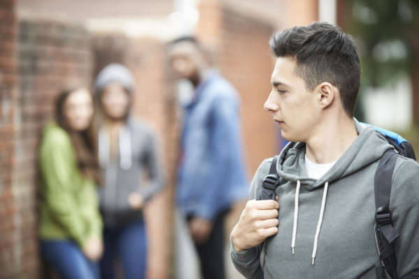 Student walking with a backpack and looking over his shoulder at a group of three other students hanging out