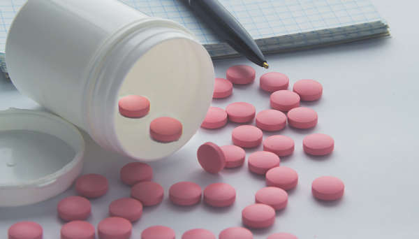 Pink pills spilling out of a small plastic container