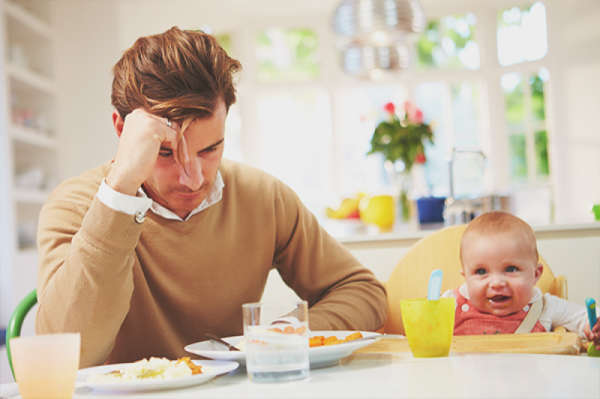 Father sitting at kitchen table with baby in high chair