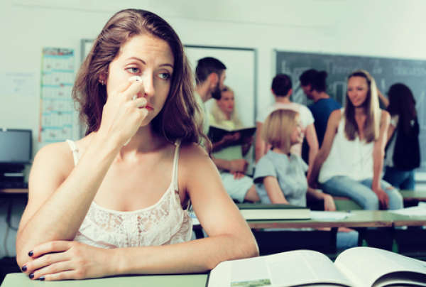 悲伤的女大学生坐在教室里，远离其他学生