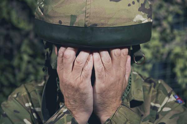 soldier dress in combat fatigues, holding hands over their eyes and face, looking dejected